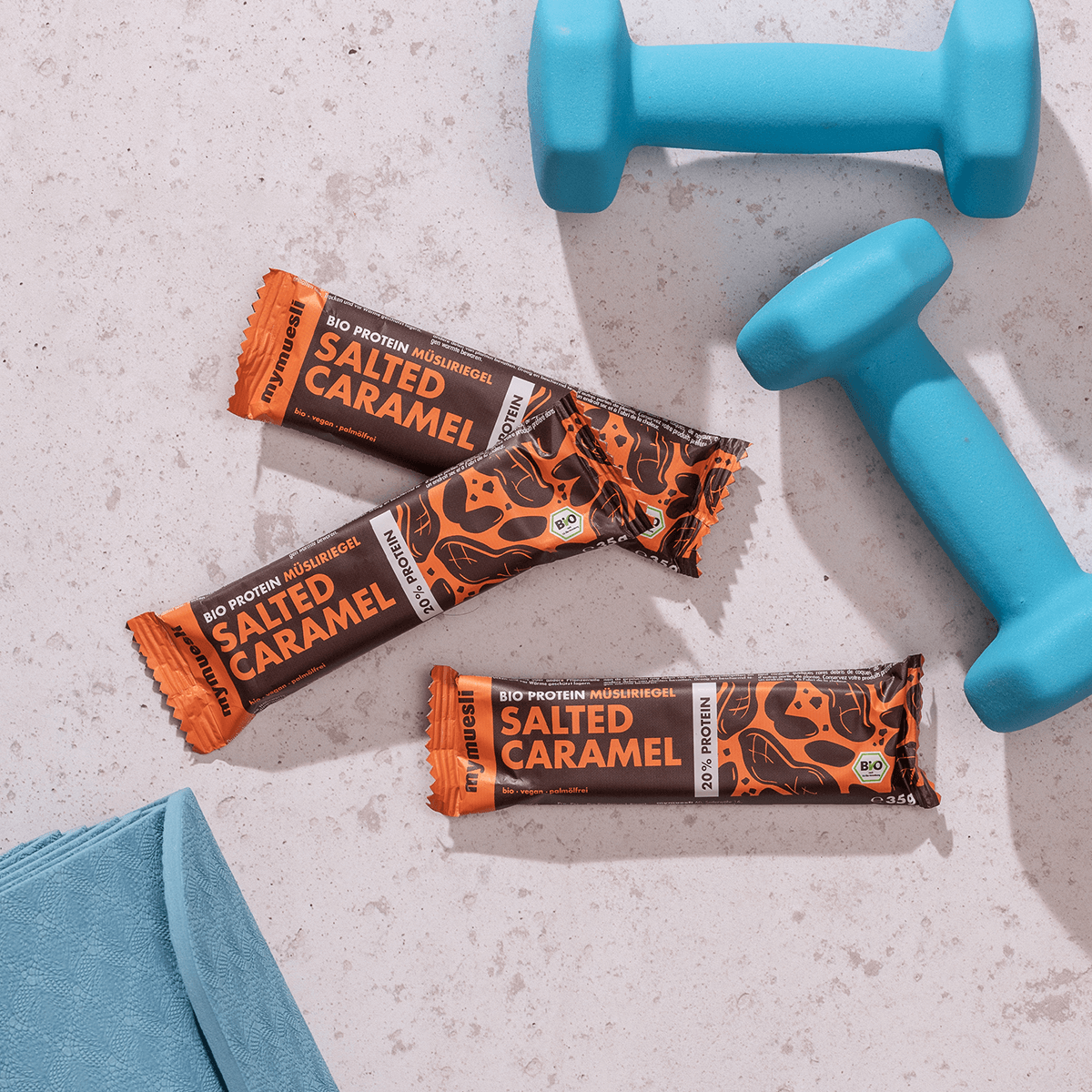 mymuesli Bio Protein Müsliriegel Salted Caramel umgeben von Kurzhanteln und Yogamatte.