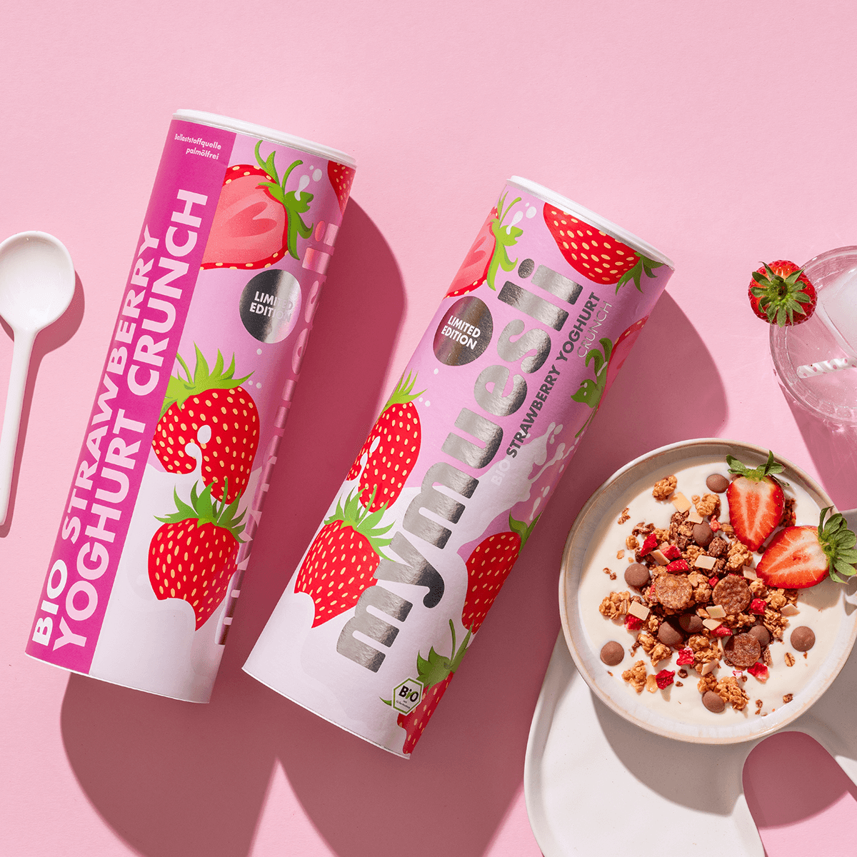 mymuesli Bio Strawberry Yoghurt Crunch Müsli in Schale mit Joghurt und frischen Erdbeeren neben Dosen