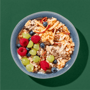 Schüssel mit Bircher, geriebenem Apfel, Beeren und Trauben