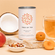 Tree of Tea Peachy June neben einem Glas Tee, Pfirsichen und einer halben Kokosnuss