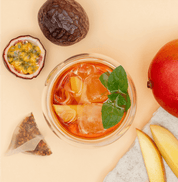 Tree of Tea Ice Tea Mango Passionfruit im Glas mit einer Mango und Passionsfrucht daneben