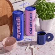 Zwei Vorratsdosen blau & rosa stehend neben einer Tasse und Schalen