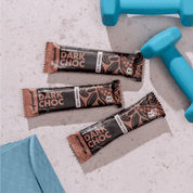 mymuesli Bio Protein Müsliriegel Dark Choc umgeben von frabenfrohen Kurzhanteln und Yogamatte.