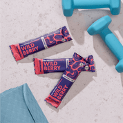mymuesli Bio Protein Müsliriegel Wild Berry umgeben von frabenfrohen Kurzhanteln und Yogamatte.