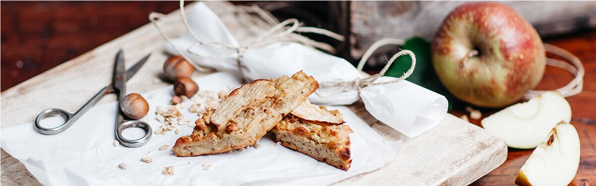 Fruchtiger Müsliriegel auf einem Backpapier mit einem Apfel dahinter