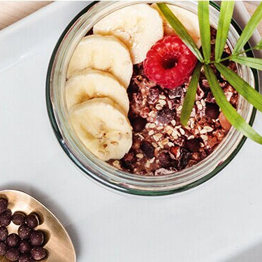 Banane Schoko Overnight Oats in einem Glas mit Bananenscheiben und einem Löffel daneben