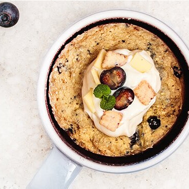 Blueberry Tassenkuchen in einer Schale mit Heidelbeeren und goldenem Löffel daneben