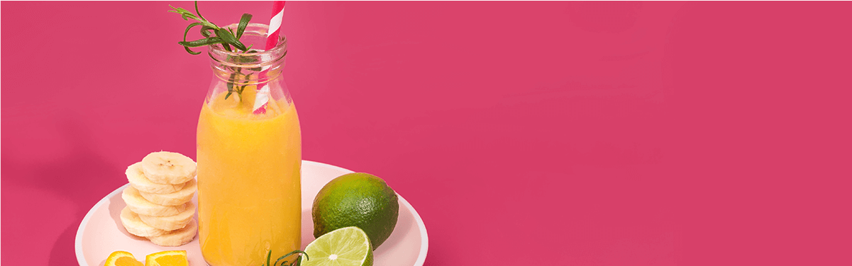 Mango Smoothie in einer Flasche und daneben Bananenscheiben und Limetten