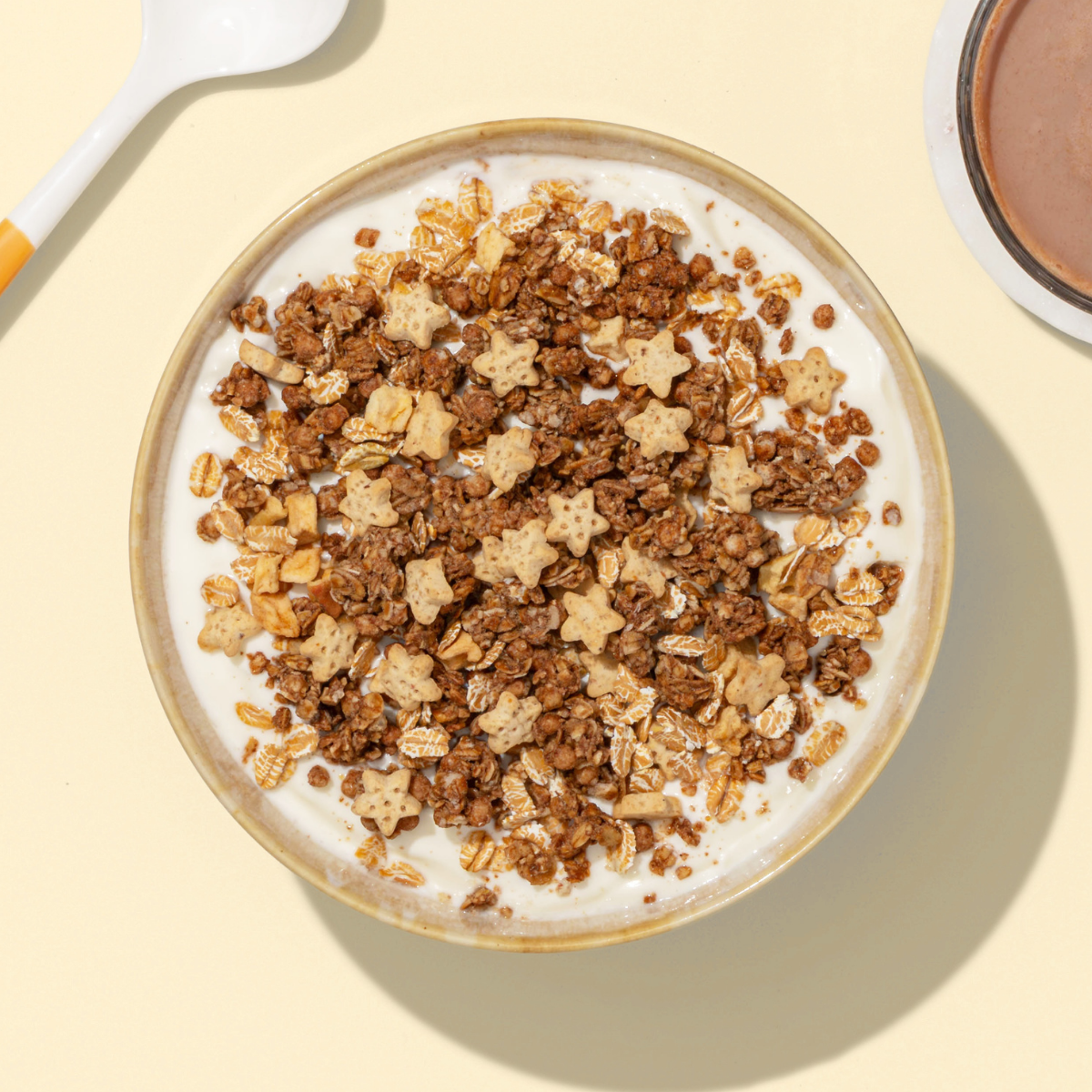 Müsli aus Schokocrunchy, Bratapfelkekse, Apfelstücke in Schüssel und neben dran ein Löffel und eine Tasse Kaffee