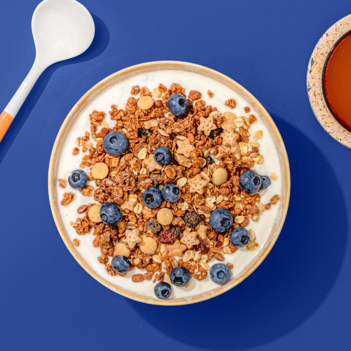 Müsli mit Crunchys, Blaubeeren und Bratapfelkesken, daneben ein Löffel und eine Tasse Kaffee