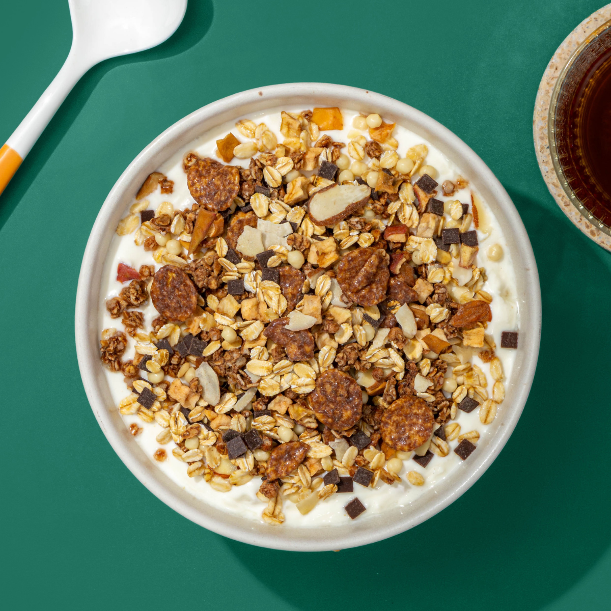 Mülsi mit Schoko Flakes, Haferflocken, Apfel- und Schokostücke, daneben ein Löffel und eine Tasse Tee