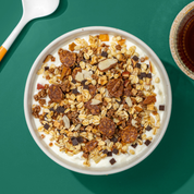 Mülsi mit Schoko Flakes, Haferflocken, Apfel- und Schokostücke, daneben ein Löffel und eine Tasse Tee