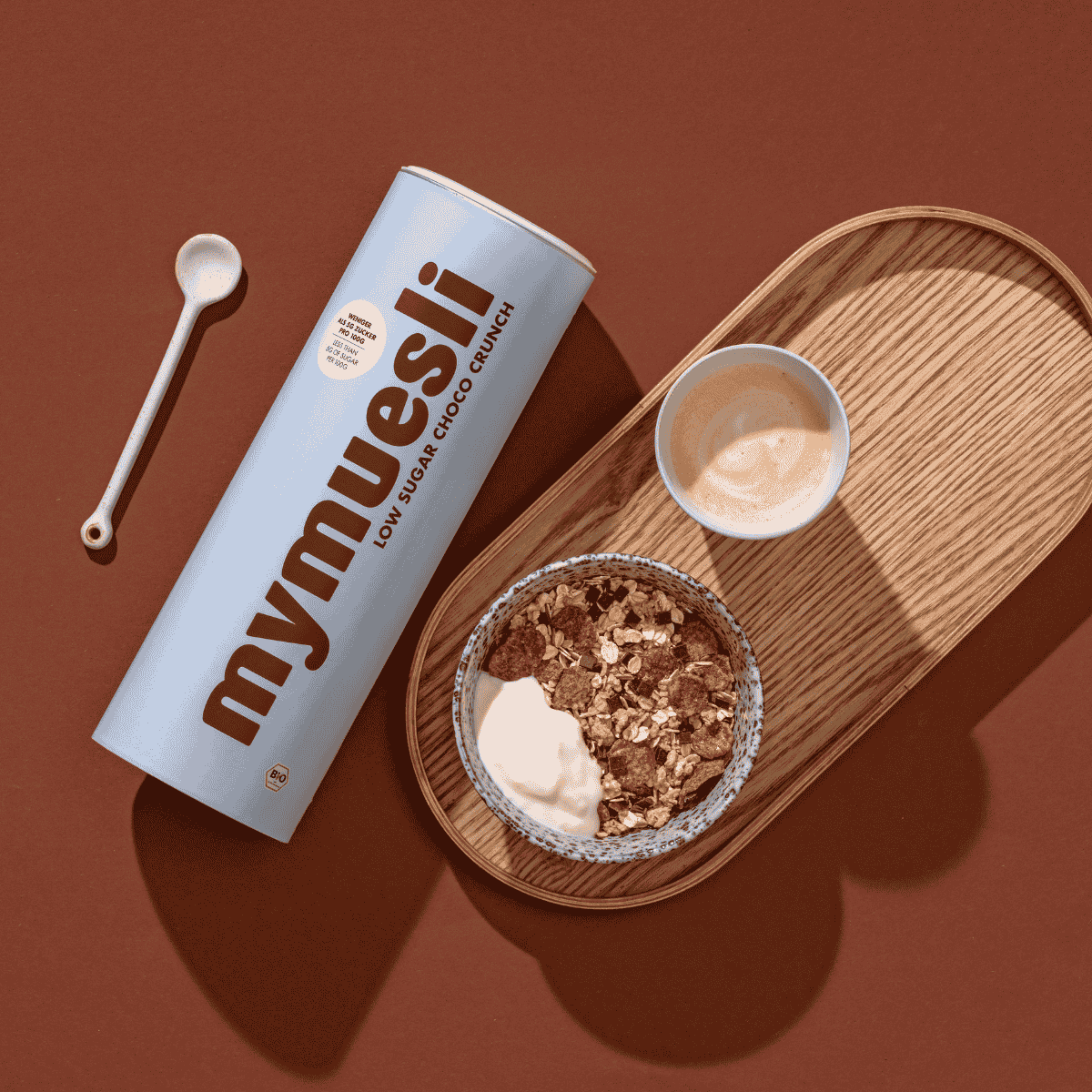 Das mymuesli Low Sugar Choco Crunch Müsli angerichtet mit frischem Joghurt auf einem Holz Brett als Teil des Feel Good Bundles.