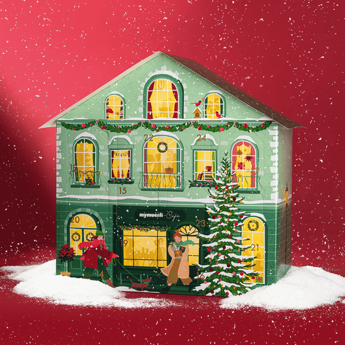 Grünes Adventskalenderhaus mit leichtem Schnee und weihnachtlicher Dekoration. Vor dem Haus läuft eine Frau mit ihrem Dackel vorbei. Ein Mann steht auf der Leiter und schmückt einen Tannenbaum. Die Fenster des Hauses sind beleuchtet. 