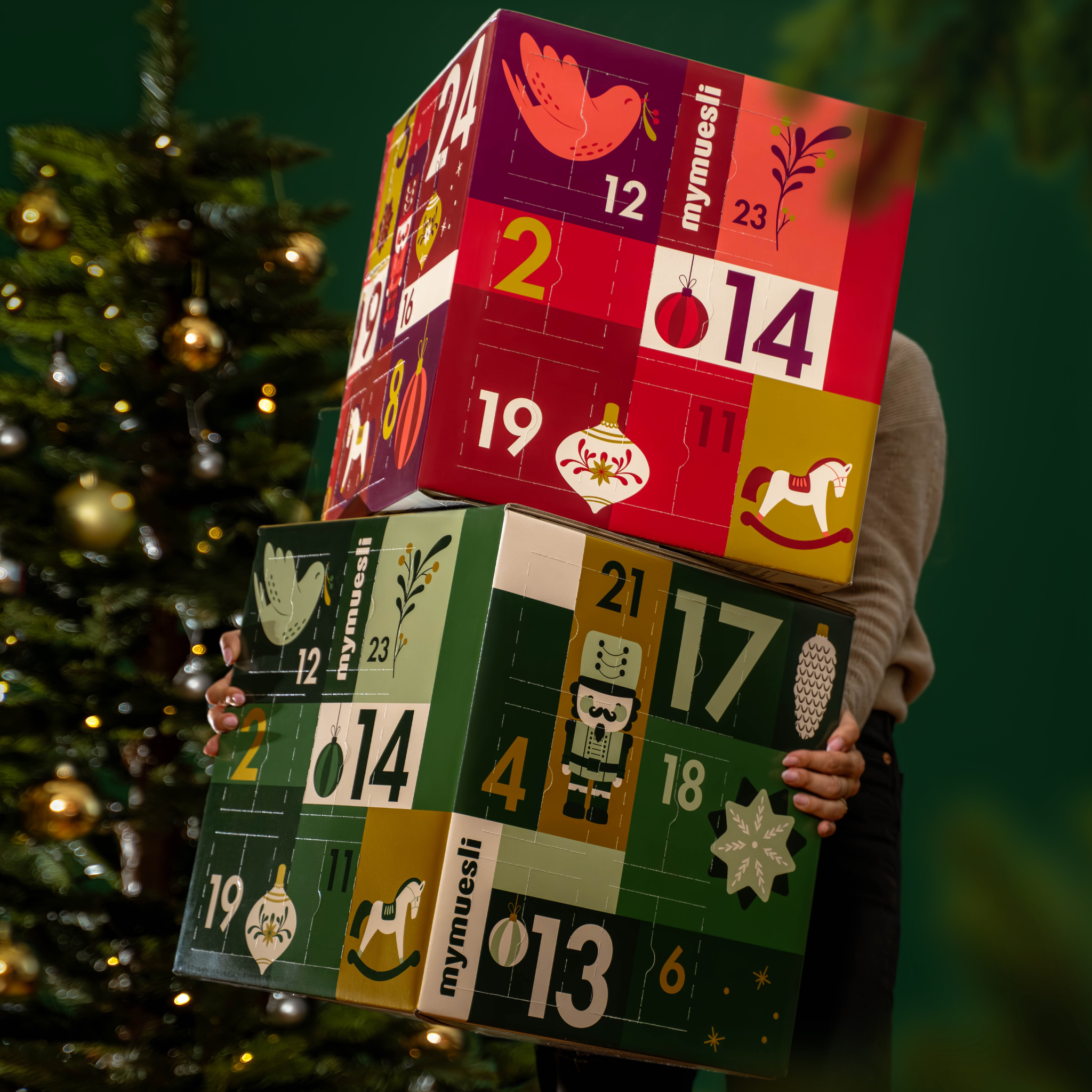 mymuesli Bio Müesli und Porridge Adventskalender, getragen von einer Frau in weihnachtlich grünem Hintergrund.