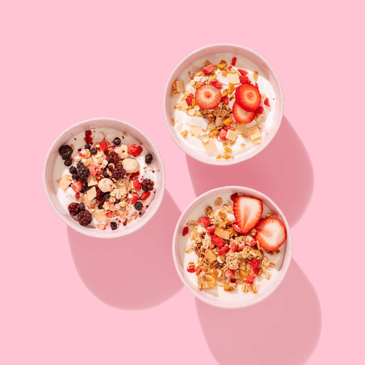 3 Müsli Schalen mit Beeren verziert auf rosanem Hintergrund. 