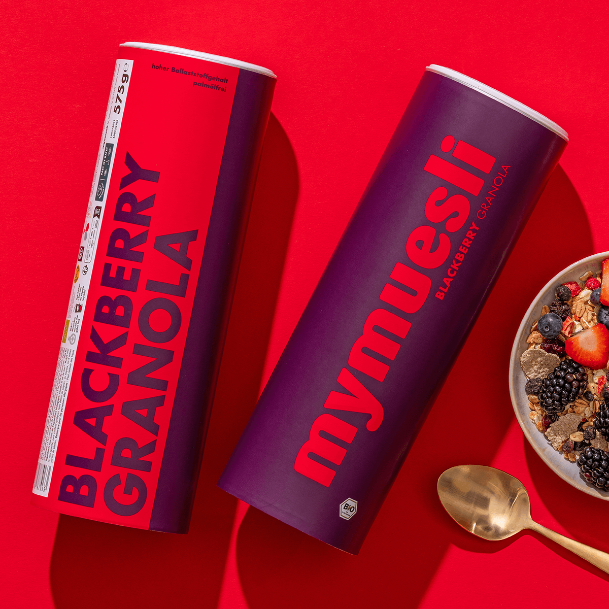 mymuesli Bio Blackberry Granola Dosen mit Müslischale mit frischen Beeren und goldenen Löffel