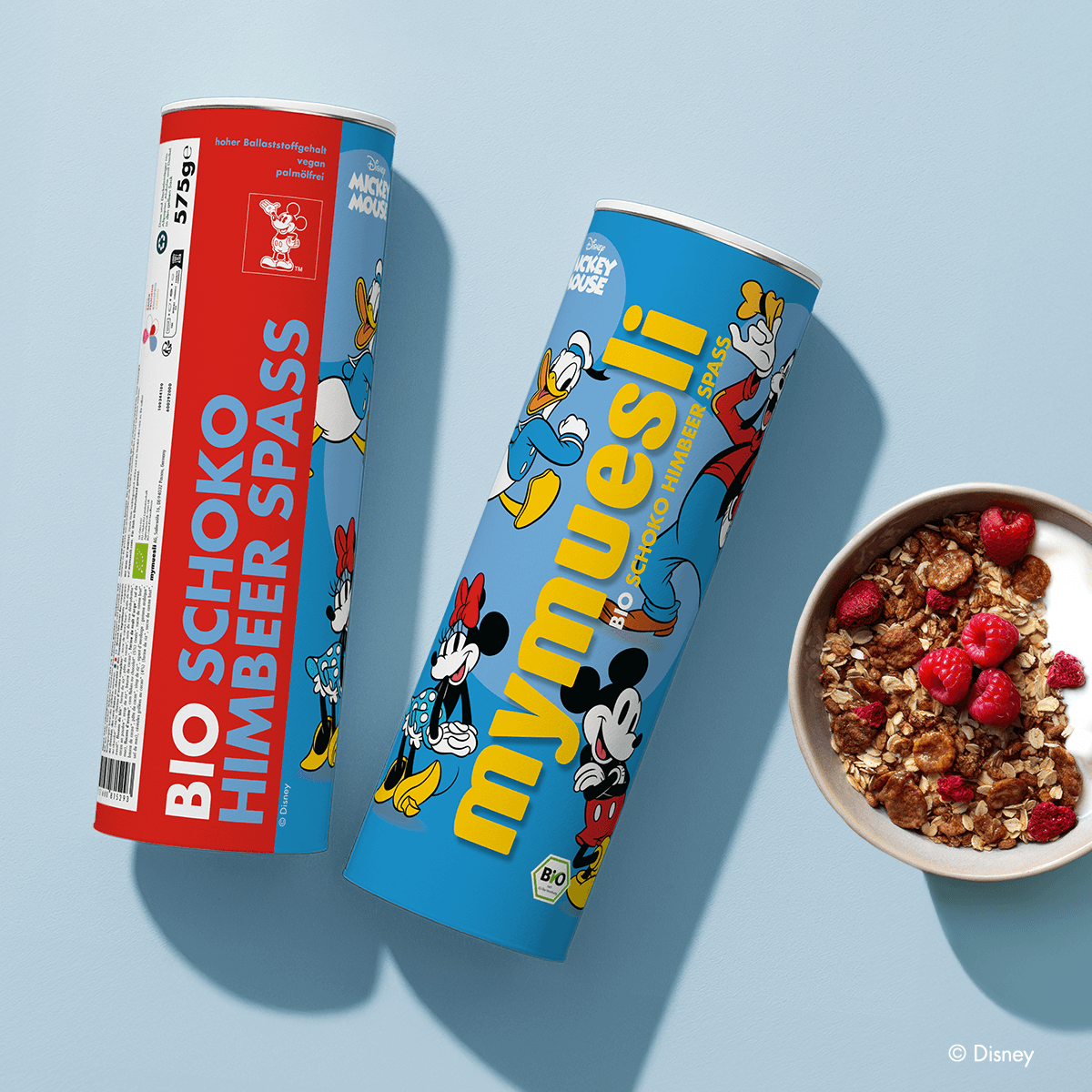 mymuesli Disney Schoko Himbeer Spaß Dosen neben Schale mit Müsli und Joghurt