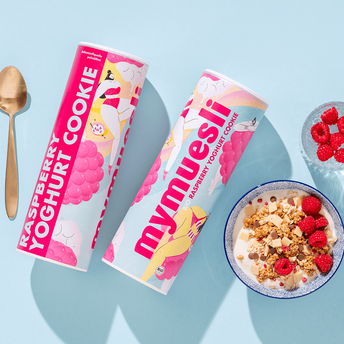 mymuesli Bio Raspberry Yoghrut Cookie In Schale mit Yoghurt und frischen Himbeeren neben Dosen von Vorne und der Seite