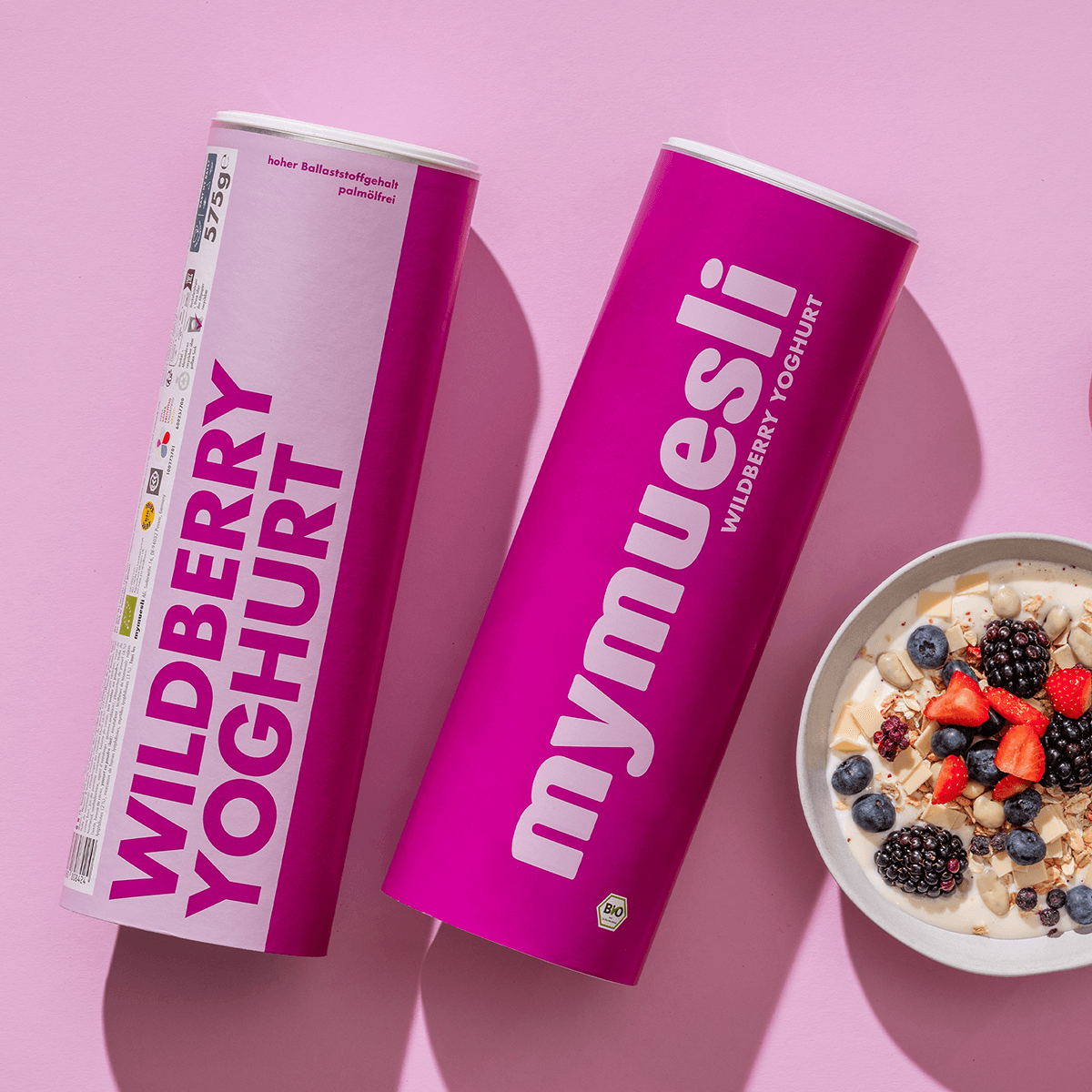 mymuesli Bio Wildberry Yoghurt in pinker Verpackung, mit Brombeeren, Erdbeeren und Blaubeeren auf Joghurt.