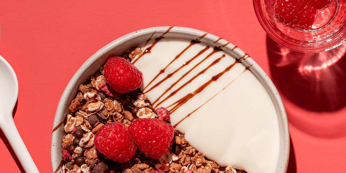 mymuesli Bio Raspberry Dark Choc Müsli in Schale mit frischen Himbeeren, Joghurt und Schokoladensauce