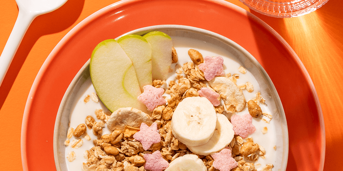 mymuesli Bio Supermaus Müsli in Schale mit Joghurt, frischen Apfelscheiben und Banane