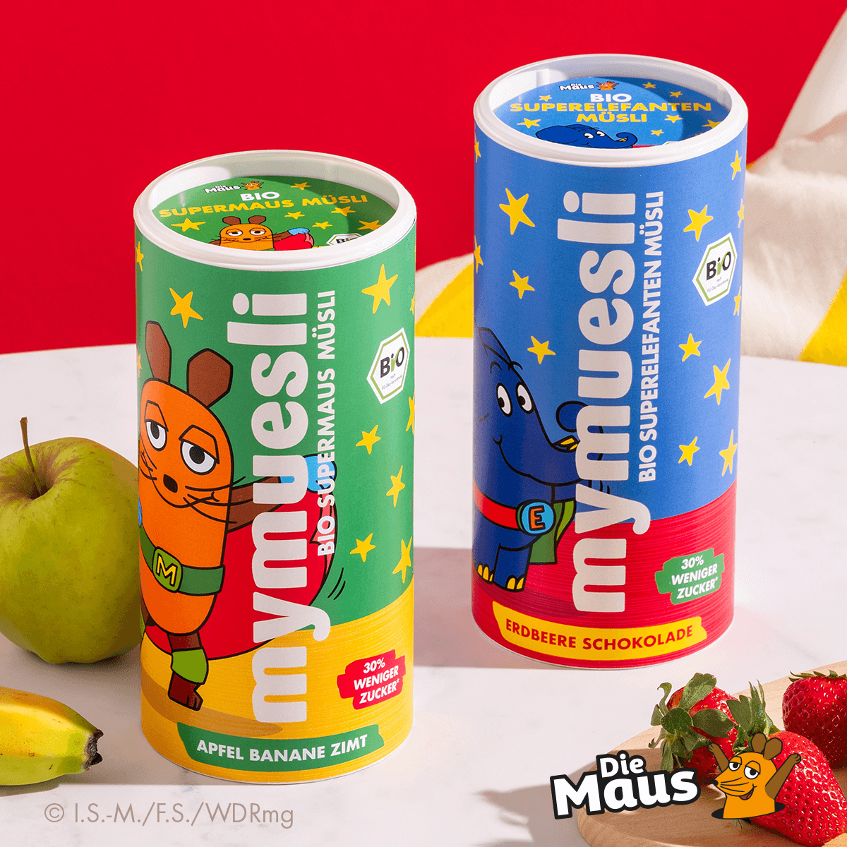 mymuesli Bio Supermausmüsli in Dose neben Apfel und Bio Superelefantenmüsli vor Erdbeeren