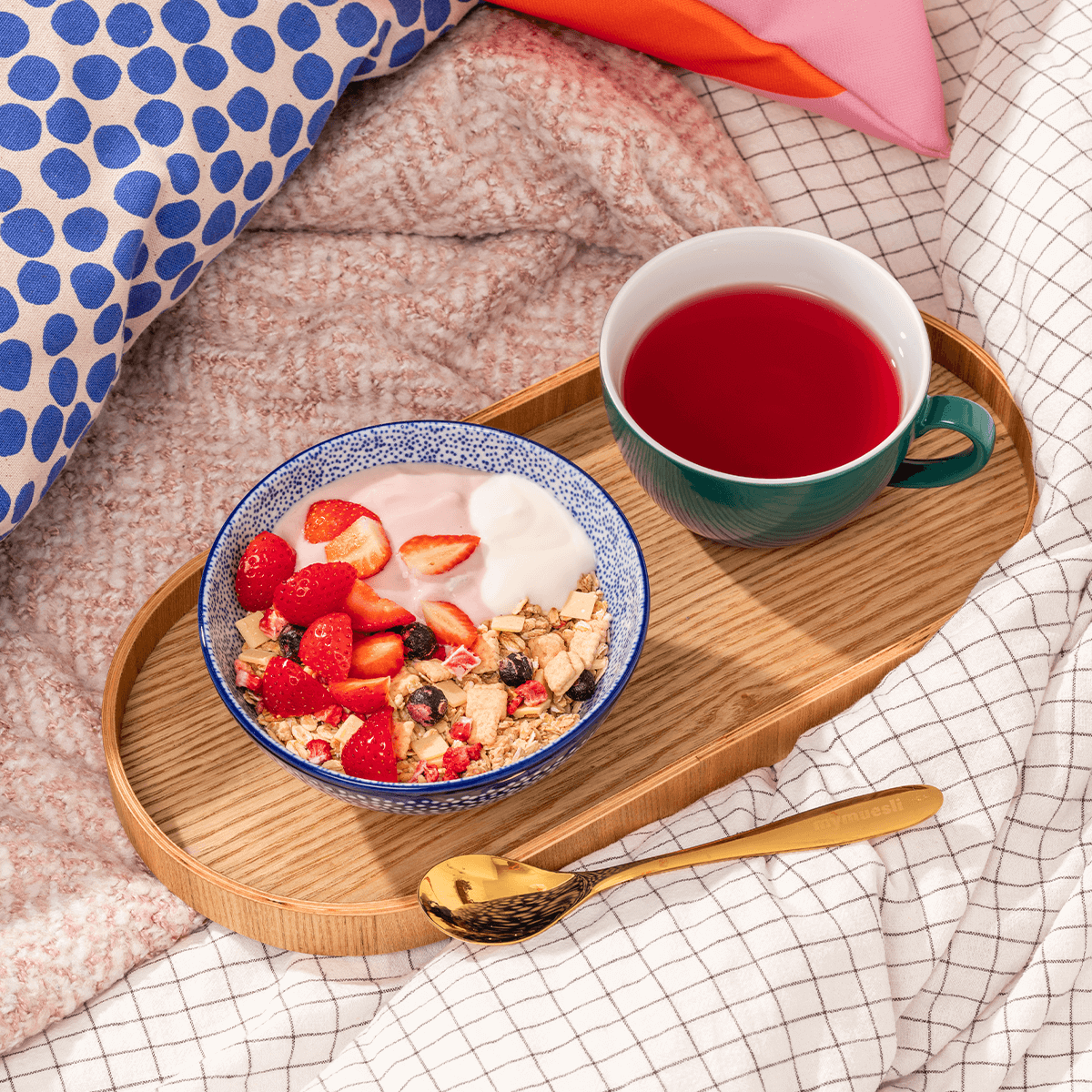 mymuesli Frühstück im Bett: Strawberry Cheesecake Müsli in Schale mit Joghurt und frischen Erdbeeren auf Tablett mit Tee 