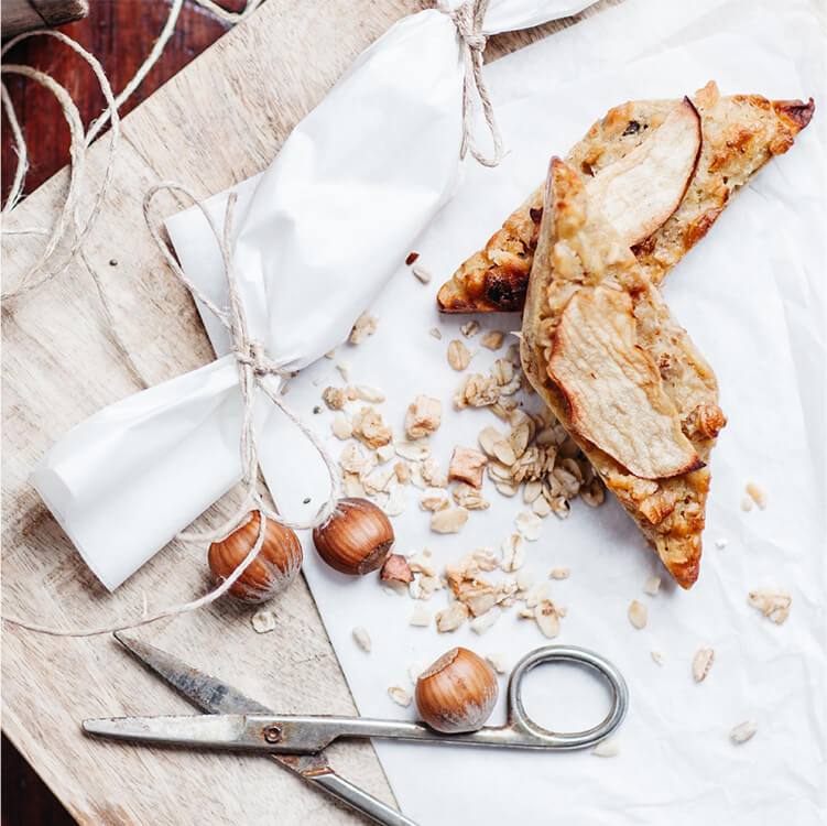 Fruchtiger Müsliriegel auf einem Backpapier mit einem Apfel dahinter