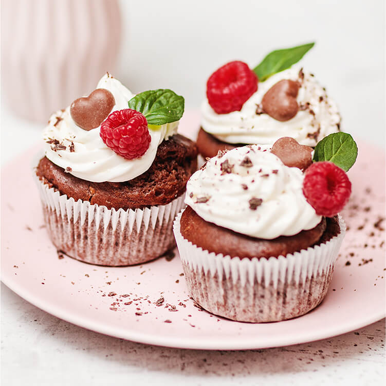 Schoko Muffins auf einem Teller mit Himbeeren und Sahne dekoriert