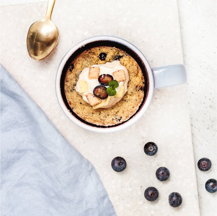 Blueberry Tassenkuchen in einer Tasse mit Heidelbeeren und goldenem Löffel daneben