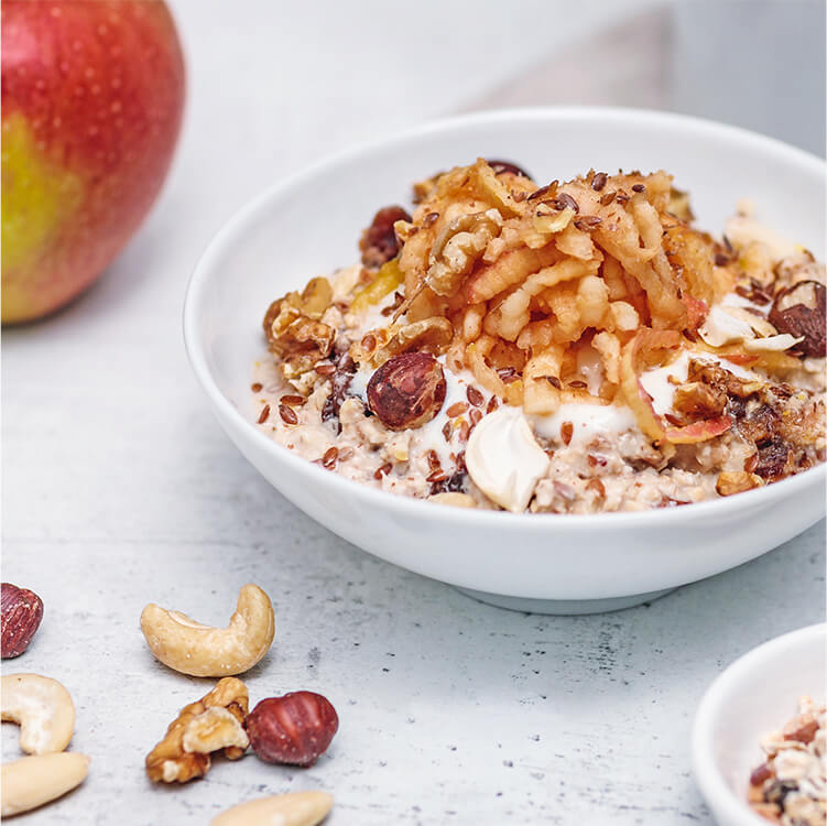 Bircher Müsli in einer Schale mit einem Apfel daneben