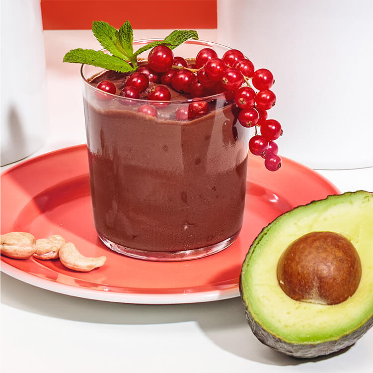 Mousse au Chocolat in einem Glas mit Cashews und Johannisbeeren dekoriert und einer halben Avocado daneben