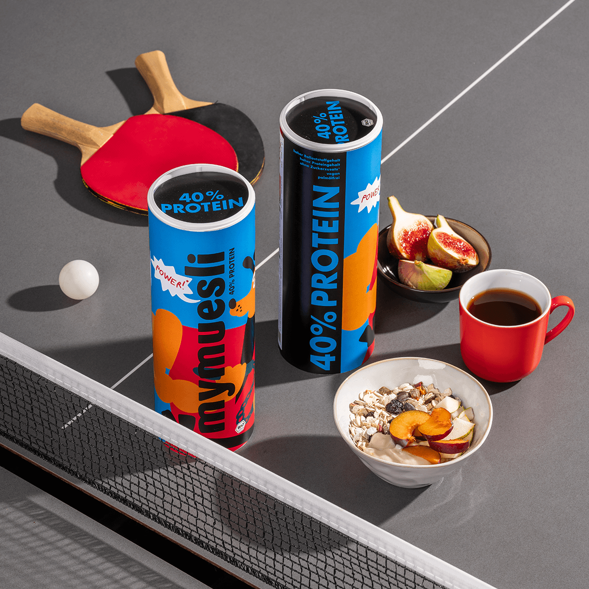 mymuesli 40% Proteinmüsli auf Tischtennisplatte mit Müslischale, frischen Feigen und Kaffee
