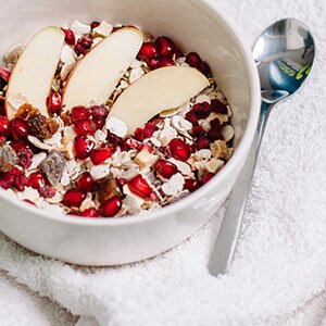 Eine Schale mit Granatapfelkernen, Apfelspalten und Müsli