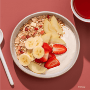 Disney Guten Morgen Löwe Müsli in einer Müslischale mit Bananenscheiben, Erdbeeren, Apfelspalten und Joghurt.