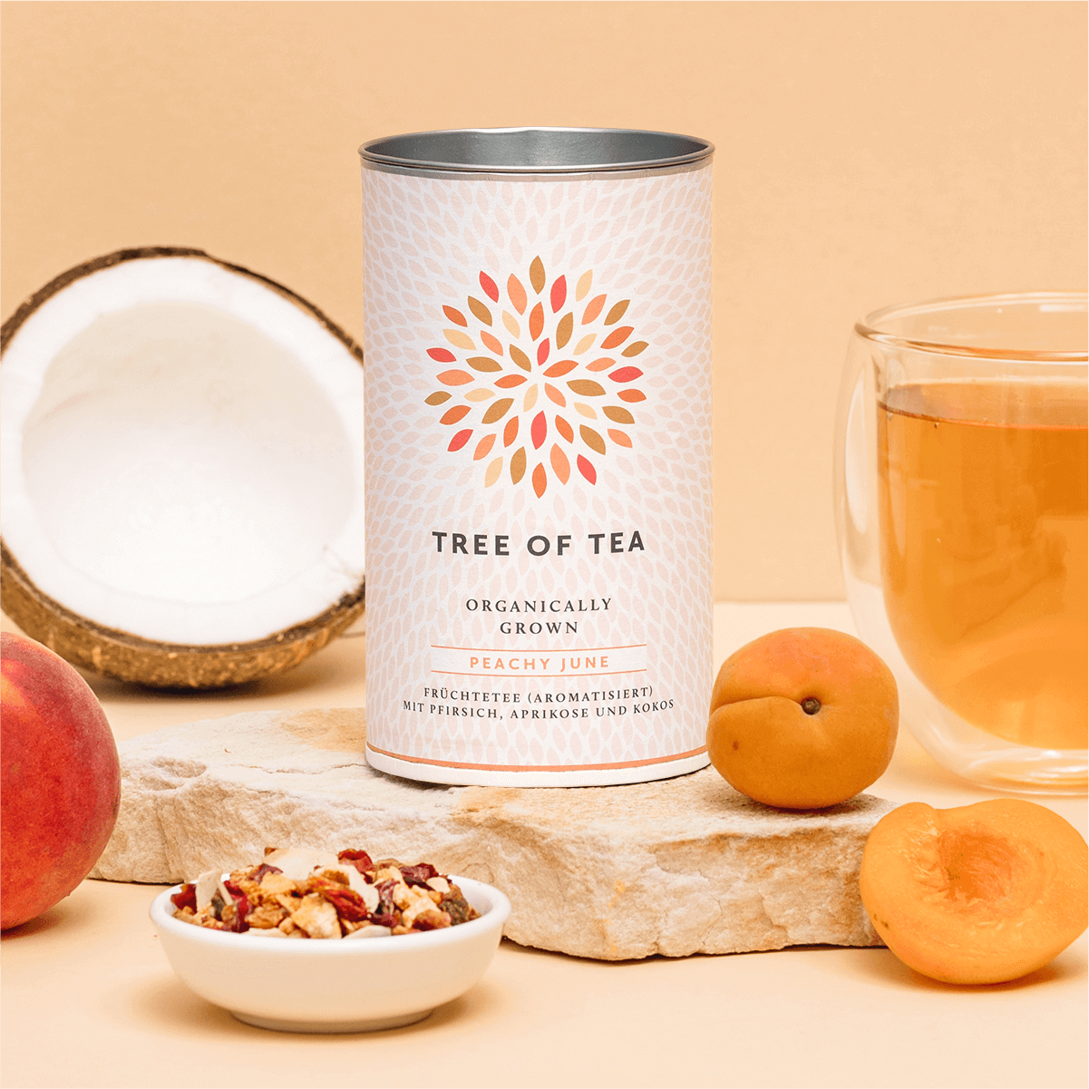 Tree of Tea Peachy June neben einem Glas Tee, Pfirsichen und einer halben Kokosnuss