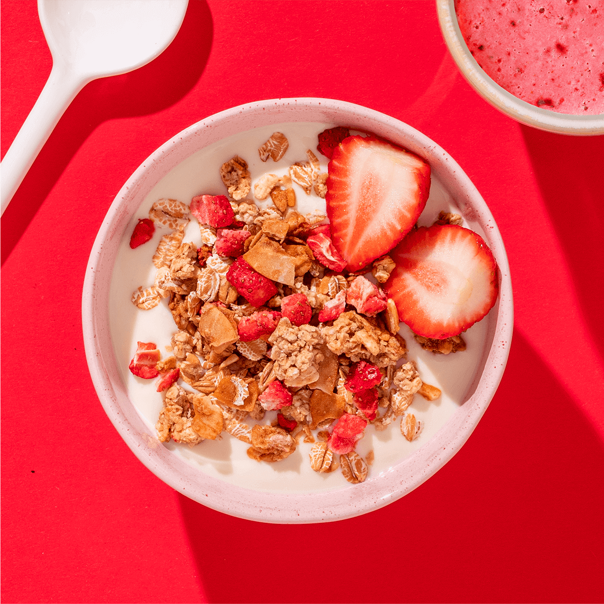 mymuesli Bio Pink Strawberry Crunchy in Schüssel mit Joghurt und frischen Erdbeeren serviert mit Erdbeer Smoothie