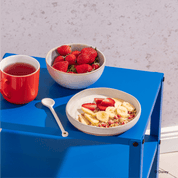 Disney Guten Morgen Löwe Müsli in einer Müslischale mit Bananenscheiben, Erdbeeren, Apfelspalten und Joghurt, daneben eine Schale Erdbeeren und ein Tee
