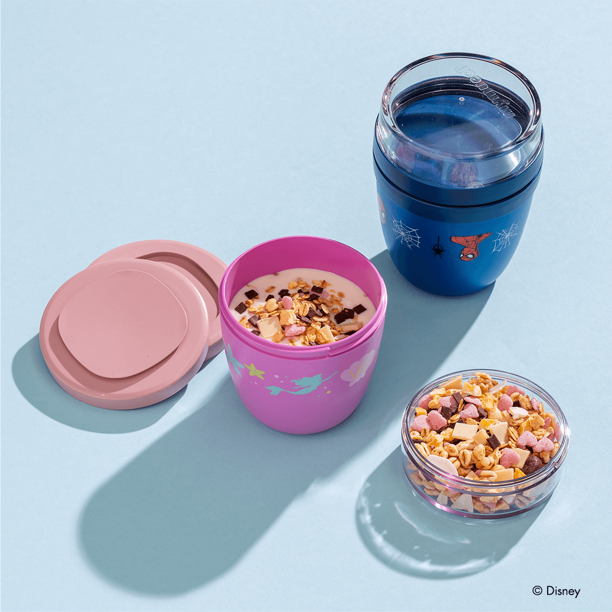 Ein leerer Spiderman Mini 2Go Becher und daneben ein Disney Princess Mini 2Go Becher, der mit Joghurt und Müsli gefüllt wird