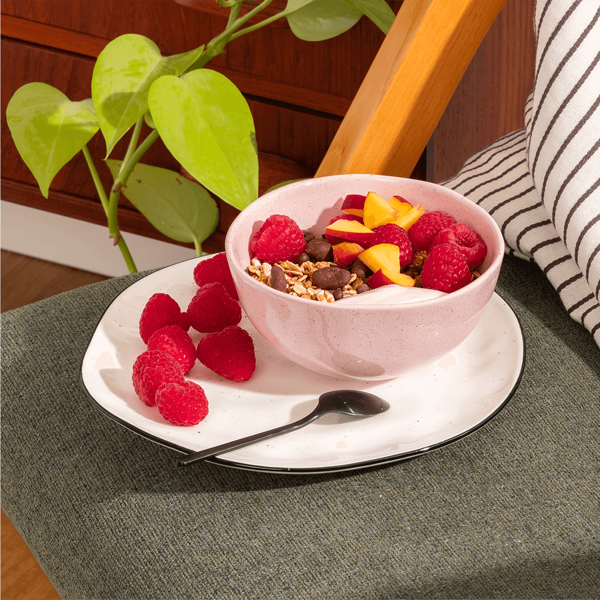 mymuesli Bio Raspberry Dark Choc müsli wird in einer Schale zusammen mit frischen Himbeeren, Pfirsichen und Yoghurt serviert. 