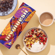Eine mymuesli Bio Herbst Müsli Dose mit herbstlichen Blättern als Design und daneben eine Schüssel Herbst-Müsli mit Johannisbeeren, Pflaumenstücken und Joghurt
