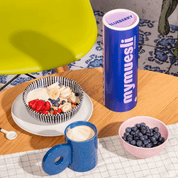 mymuesli Bio Blueberry Müsli zubereitet auf Frühstückstisch neben Dose, Kaffee und frischen Blaubeeren
