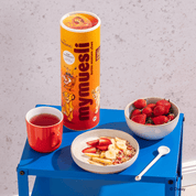 Disney Guten Morgen Löwe Müsli Dose, das Müsli in einer Müslischale mit Bananenscheiben, Erdbeeren, Apfelspalten und Joghurt, daneben eine Schale Erdbeeren und ein Tee