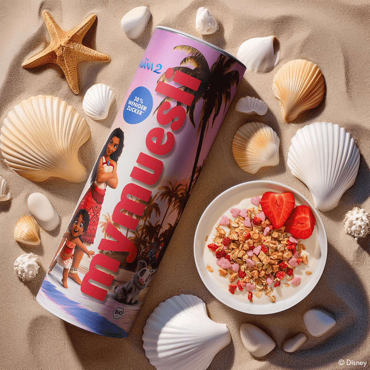 Disney Vaiana Müsli Dose neben einer Schale Vaiana Müsli mit Joghurt und Erdbeeren im Sand liegend mit Muscheln und Steinen herum